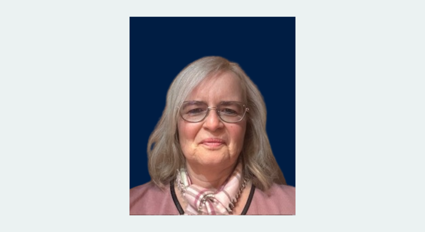 Porträt einer älteren Frau mit schulterlangem grauem Haar, Brille und rosa Schal vor blauem Hintergrund