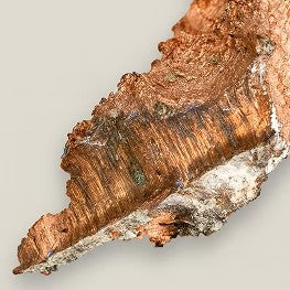 Nahaufnahme eines unregelmäßig geformten Kupferstücks mit metallisch glänzender Oberfläche.